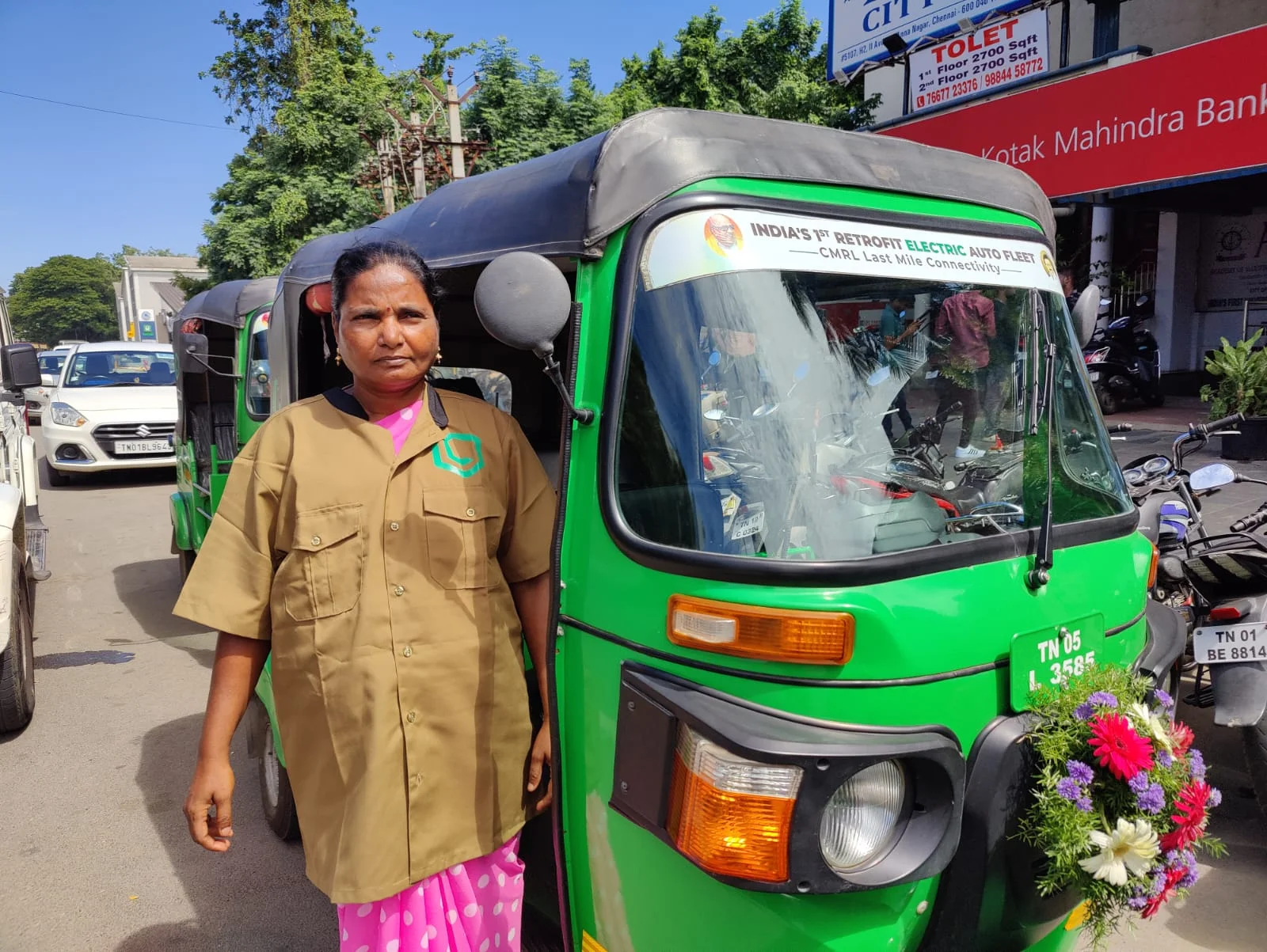 A woman driver in Leggo uniform beside her garlanded electric auto
